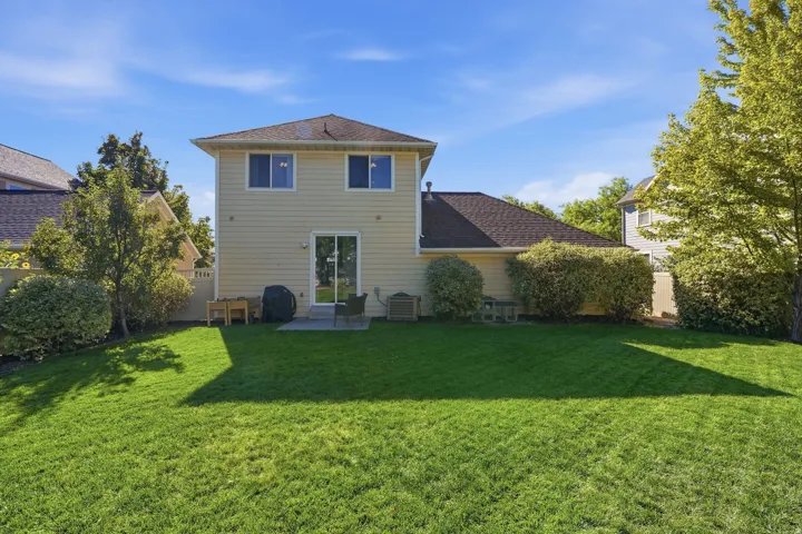 Expansive green lawn with mature landscaping, fenced perimeter, and a patio with direct access to the interior via a sliding glass door