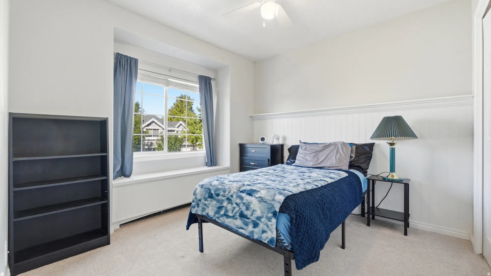 Bright bedroom with a large window, charming built-in window seat, ceiling fan, and decorative wall detail.