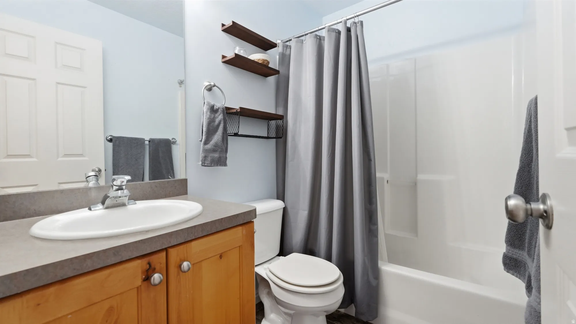 Full bathroom with tub/shower combination, vanity storage, and additional wall shelving for everyday essentials.