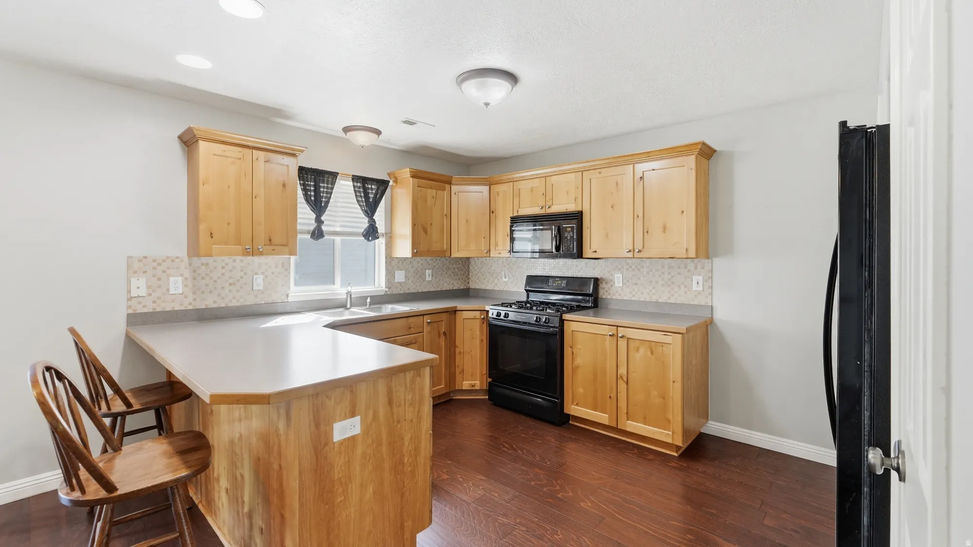Kitchen featuring wood-finish cabinetry, a peninsula with counter seating, a tile backsplash, and a black appliances