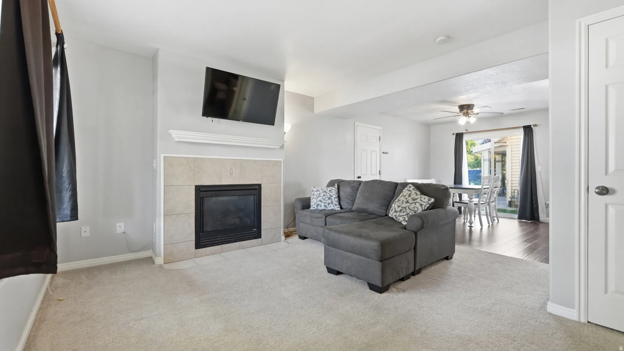 Comfortable main-level living room featuring a cozy fireplace, large windows, and an open flow into the dining and kitchen areas.