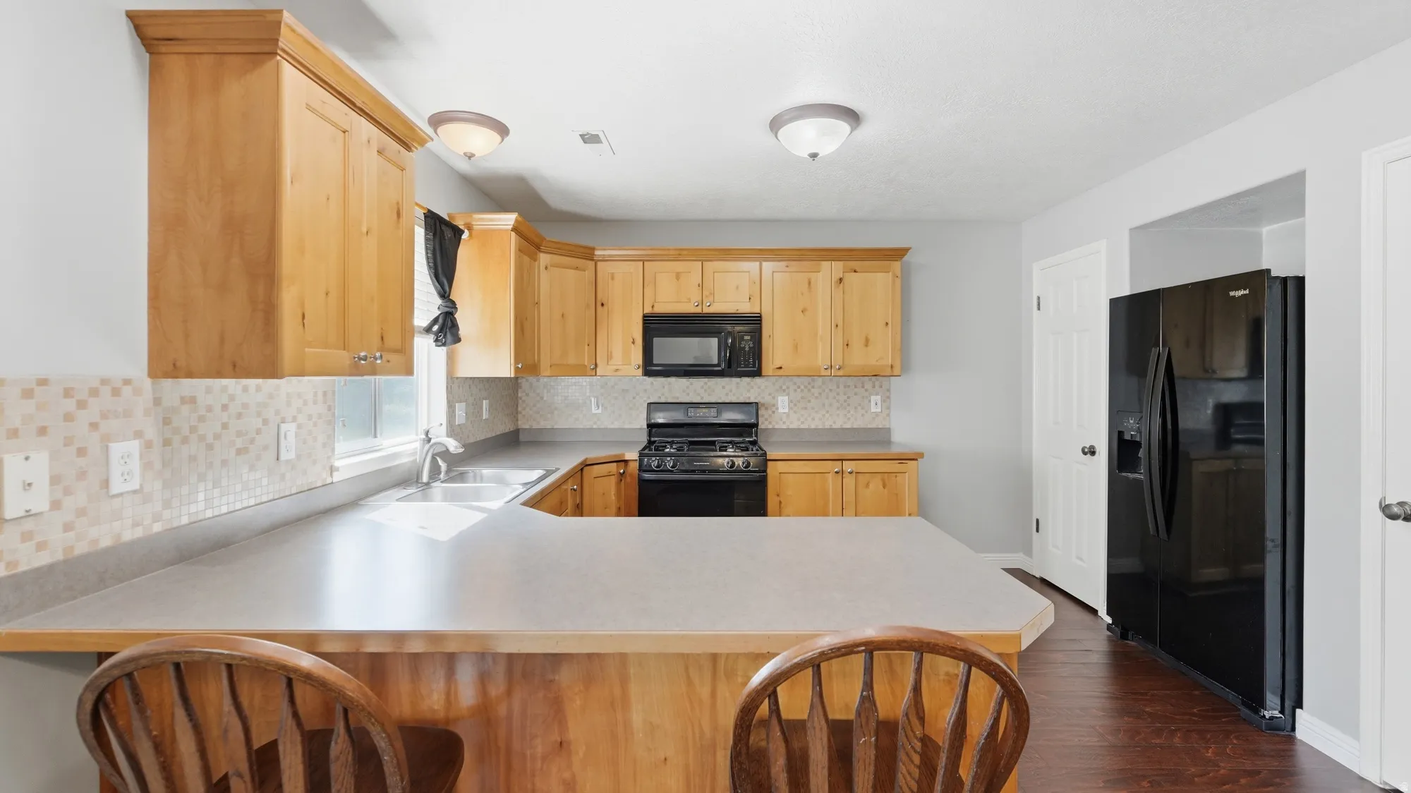 Kitchen featuring wood-finish cabinetry, a peninsula with a raised bar, a tile backsplash, and dark wood-finish flooring