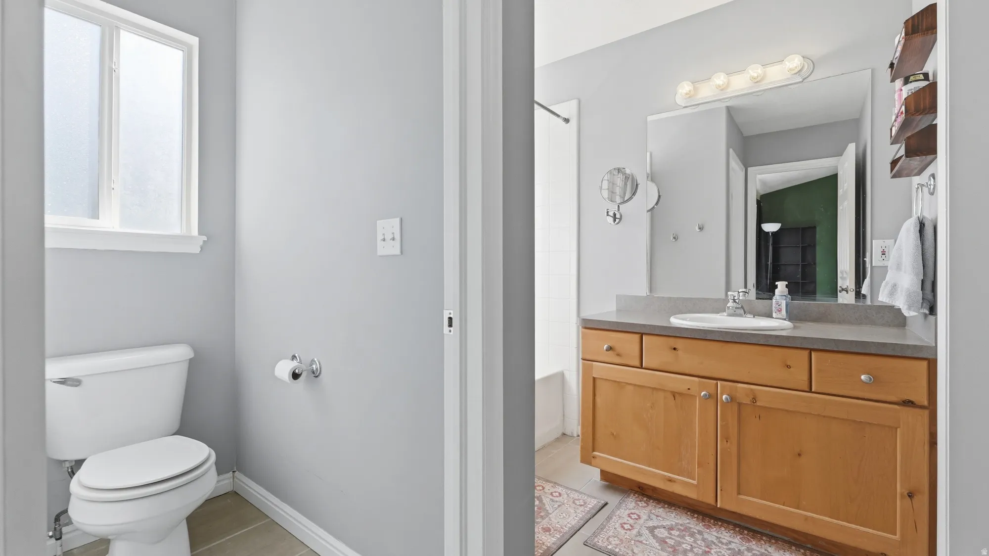 Private primary bathroom with generous vanity storage, large mirror, natural light, and separate toilet area.