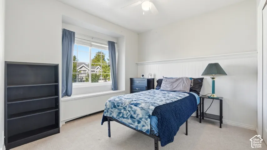 Bright bedroom with a large window, charming built-in window seat, ceiling fan, and decorative wall detail.
