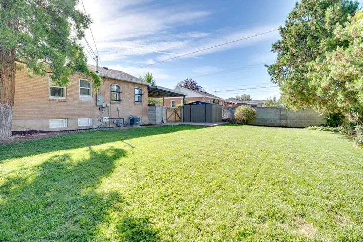 Expansive backyard featuring a manicured lawn, mature trees, and a brick exterior dwelling
