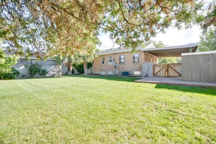 Expansive green lawn, brick exterior, covered patio, wood gate, and an attached storage shed
