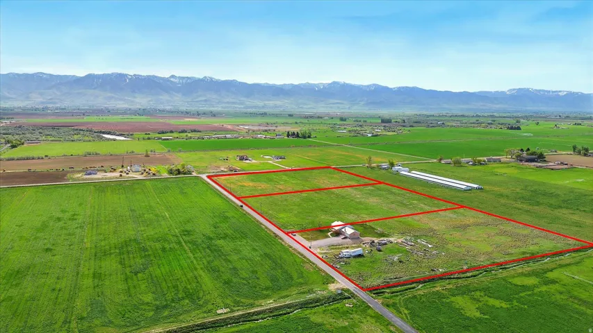 Expansive agricultural land featuring a single-story residence, multiple outbuildings, and distant mountain scenery