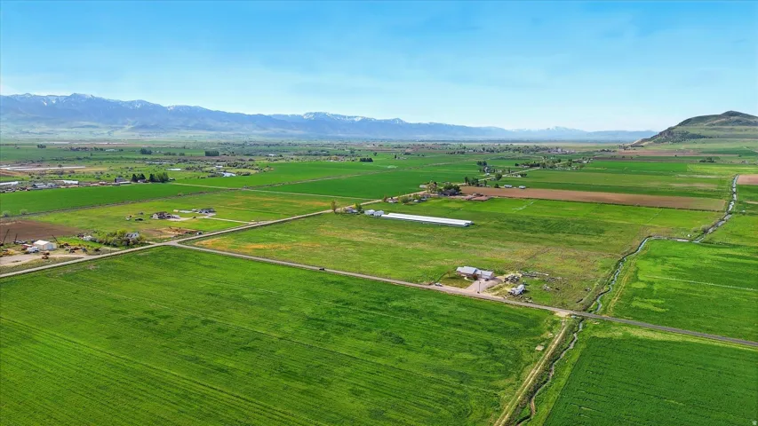 Expansive green fields, multiple outbuildings, and distant mountain ranges