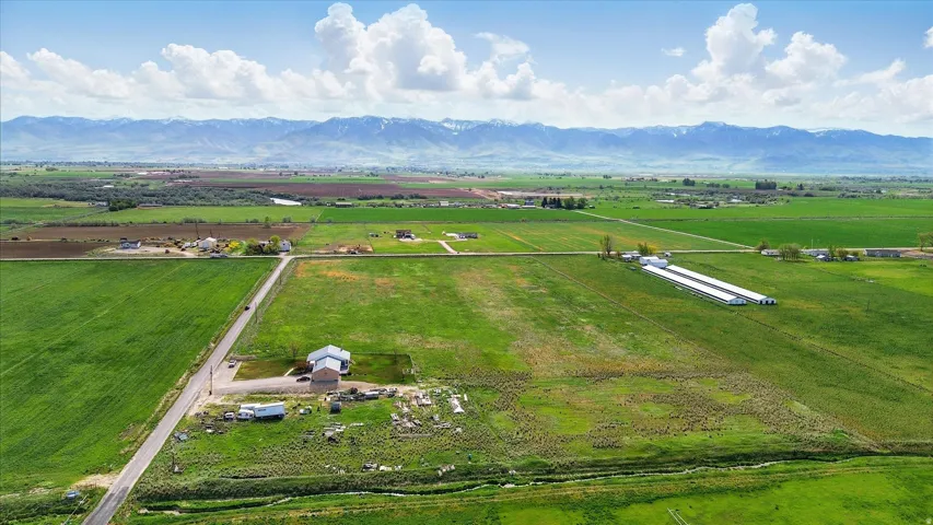 Expansive agricultural land featuring a paved road, multiple structures, and distant snow-capped mountains