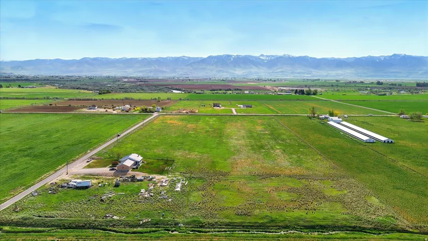 Expansive green fields, distant mountain range, scattered residential structures, agricultural buildings, and a long paved road