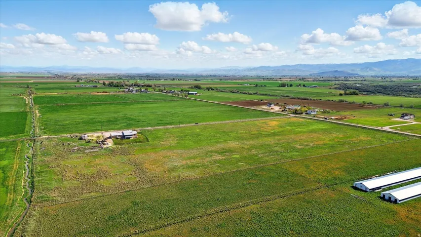 Expansive agricultural land featuring a natural water channel, multiple residential structures, and various farm buildings