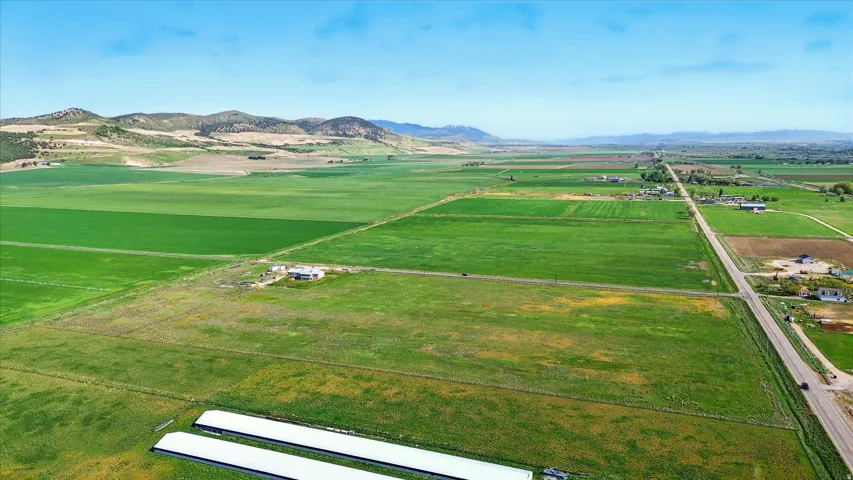 Expansive agricultural land featuring cultivated fields, distant mountain range, and a visible roadway