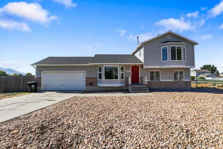 Multi-level residence featuring gray siding, a red entry door, and a two-car garage