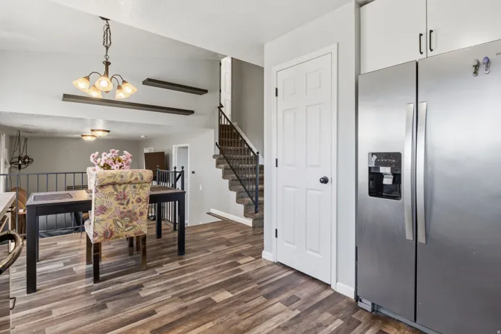 Wood-finish flooring, stainless steel refrigerator, white cabinetry with dark hardware, recessed lighting, and a staircase with black railing