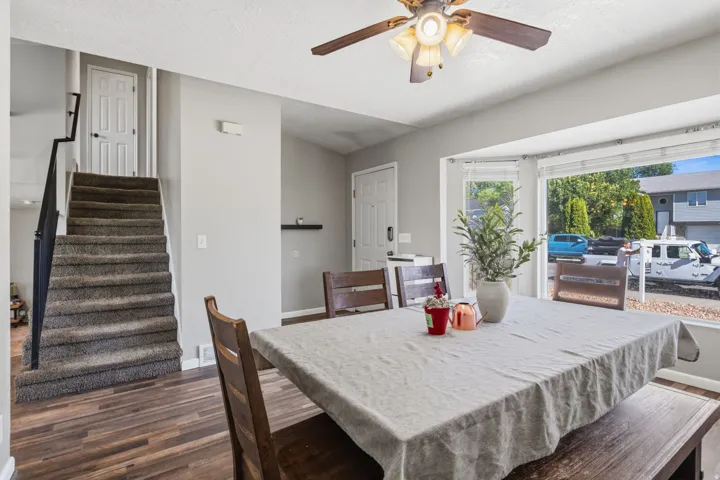Wood-finish flooring, carpeted staircase, ceiling fan with integrated lighting, and bay window