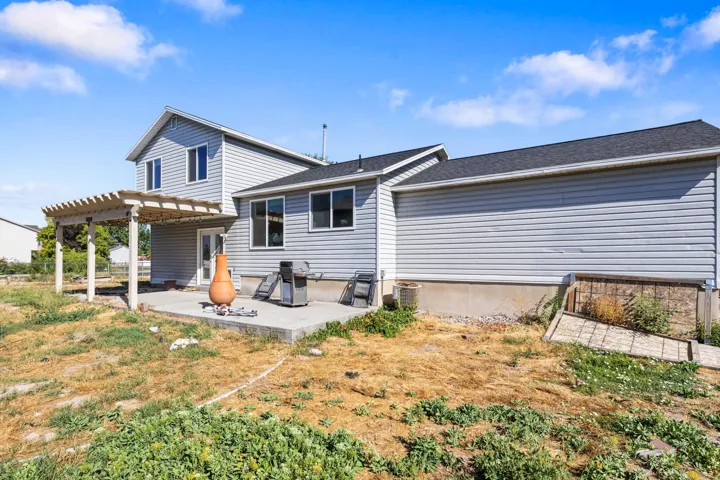 Rear exterior featuring light gray siding, dark shingle roofing, a concrete patio, and an attached wood pergola