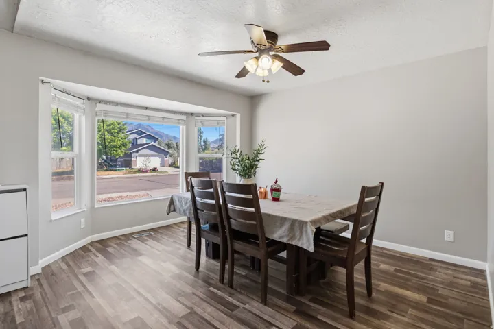 Expansive bay window, wood-finish flooring, ceiling fan with integrated lighting, neutral wall tones, and recessed lighting