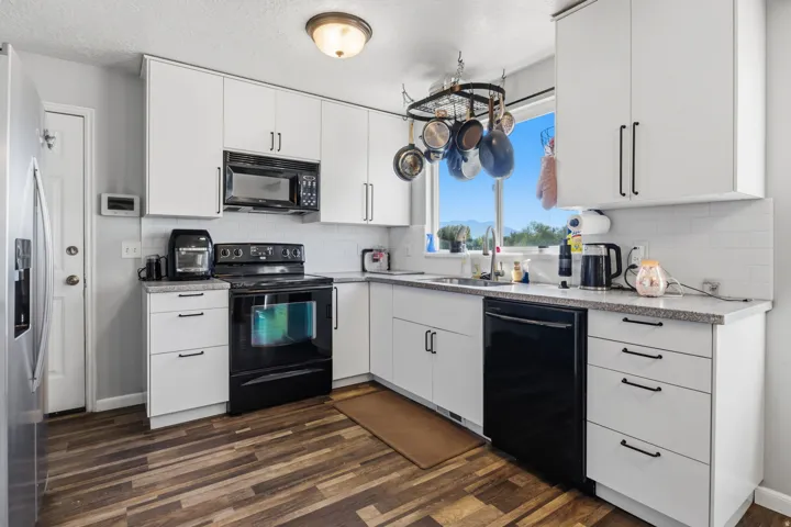 White cabinetry with matte black hardware, wood-finish flooring, white subway tile backsplash, and a stainless steel refrigerator