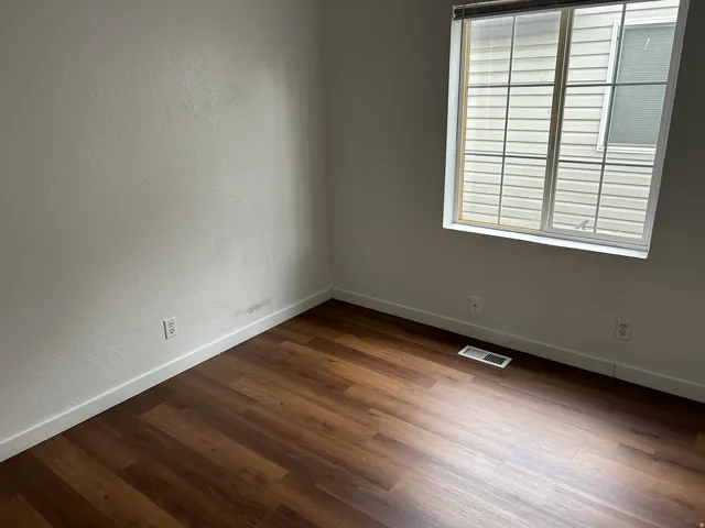 Wood-finish flooring with crisp white trim, featuring a window with horizontal blinds and a wall outlet
