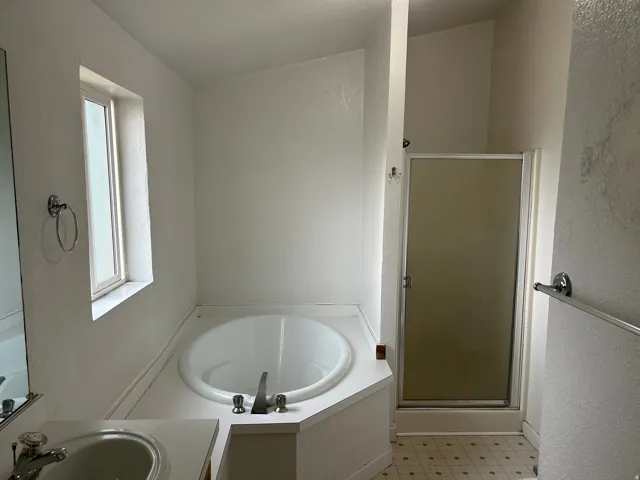 Soaking tub, enclosed shower, single basin vanity, window, and patterned flooring