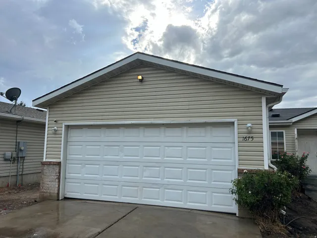 Attached garage with a panel-style door, beige siding, and a dark shingle roof