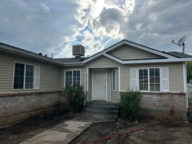 Exterior featuring beige siding, white window shutters, and a brick-finish foundation