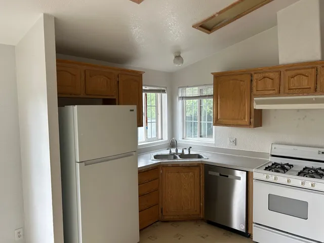 Kitchen featuring wood cabinetry, a stainless steel dishwasher, a gas range, a double basin sink, and a refrigerator