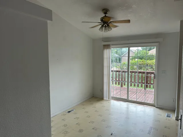 Sliding glass door leading to an outdoor deck, ceiling fan with integrated lighting, and sloped ceiling