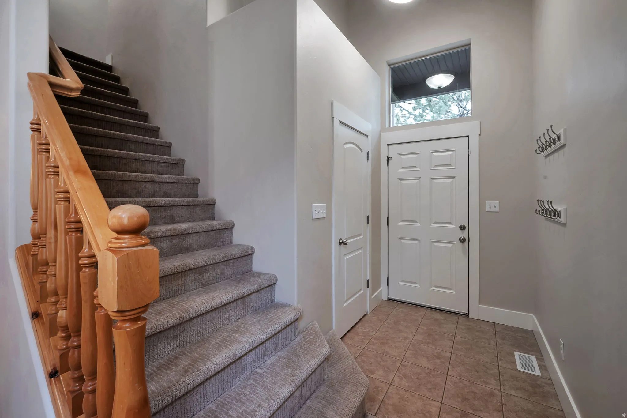 Carpeted staircase with wood banister, tile flooring, white paneled doors, and a transom window