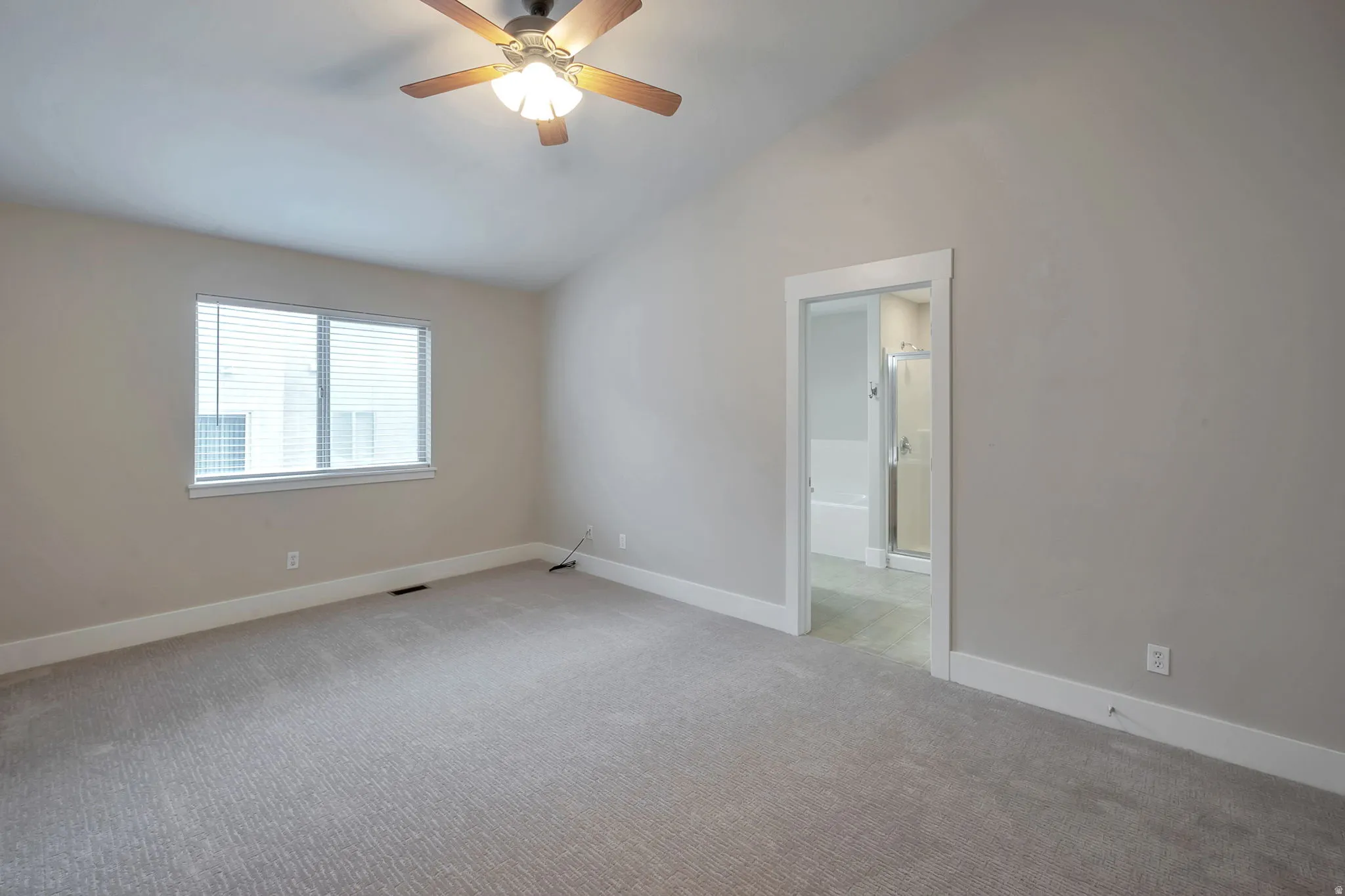 Primary bedroom with vaulted ceiling with a wood-finish ceiling fan, recessed window, light gray carpeting, and an adjoining bathroom with a shower and bathtub