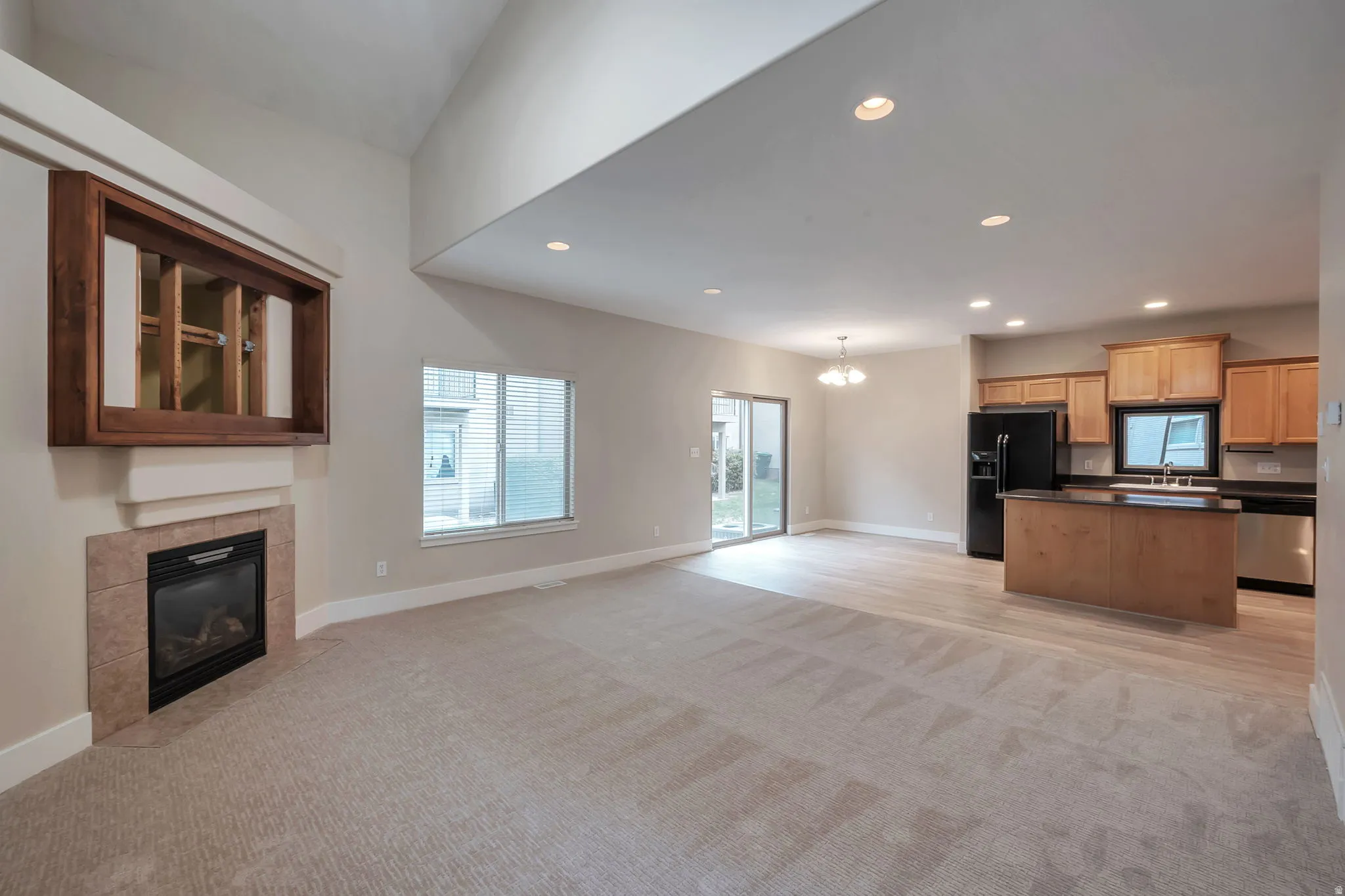 Great Room with vaulted ceiling, recessed lighting, fireplace with tile surround, wood-finish flooring, and sliding glass door