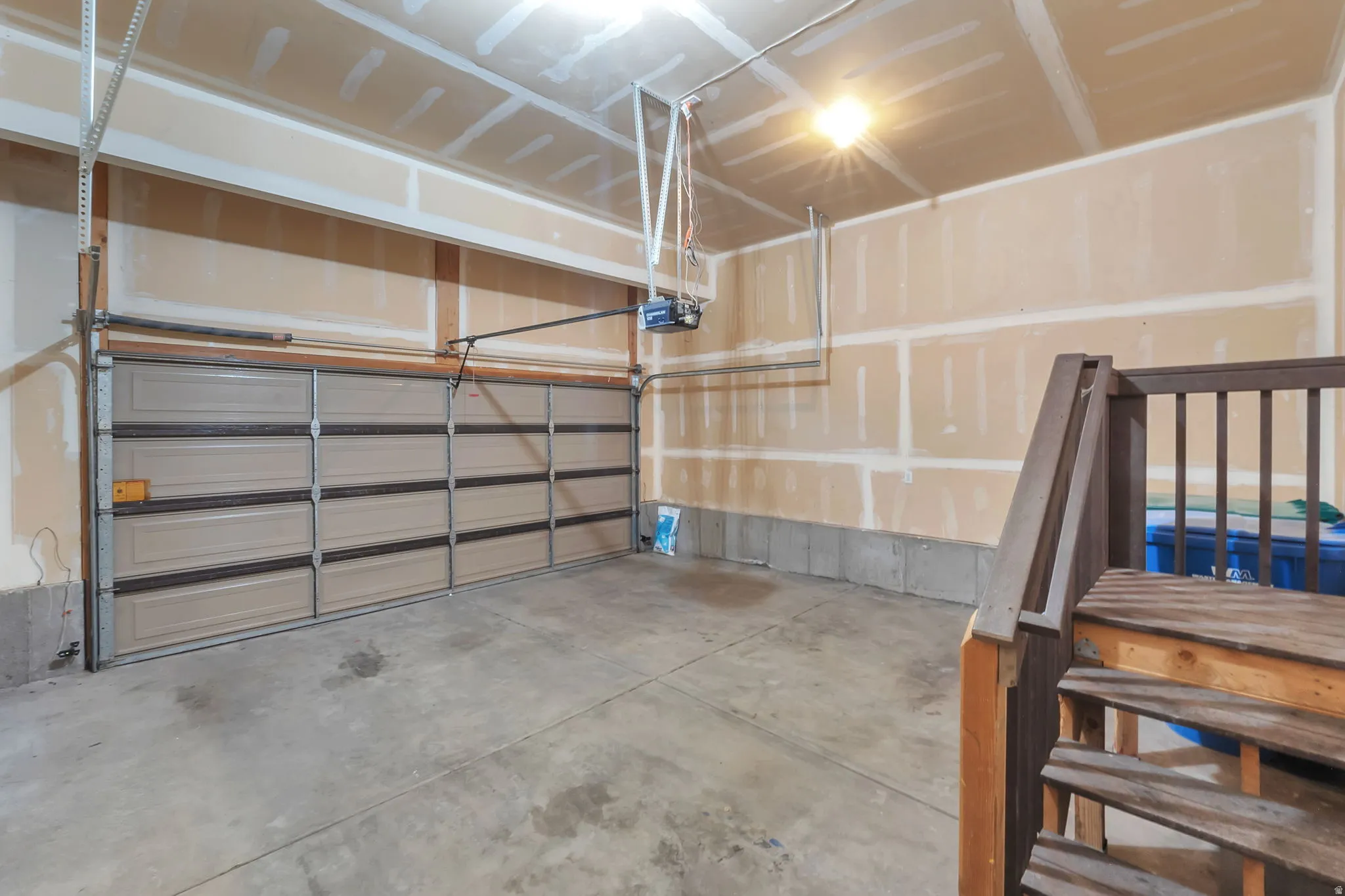 Attached garage with a panel garage door, concrete flooring, and an interior wooden staircase