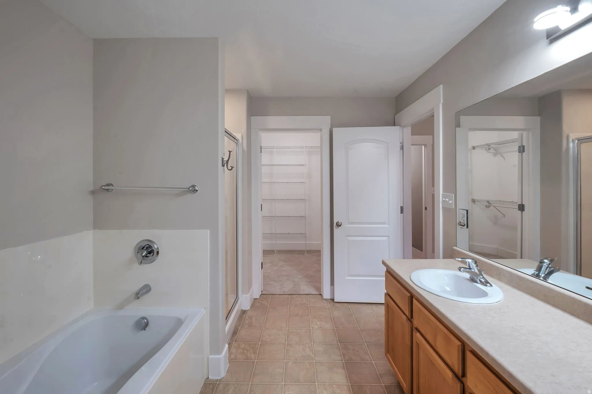 Integrated bathtub with chrome fixtures, wood-finish vanity with single basin sink, large wall-mounted mirror, and tile flooring