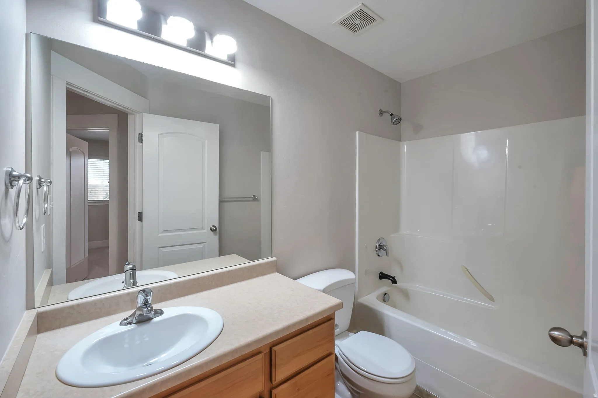 Single vanity with an integrated sink, broad wall mirror, three-light vanity fixture, and a shower-over-tub combination with a white surround