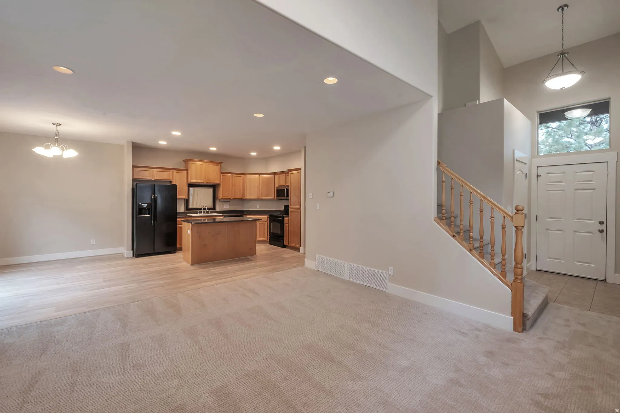 Open-concept living space with a kitchen island, wood cabinetry, recessed lighting, and a two-story entryway with a staircase