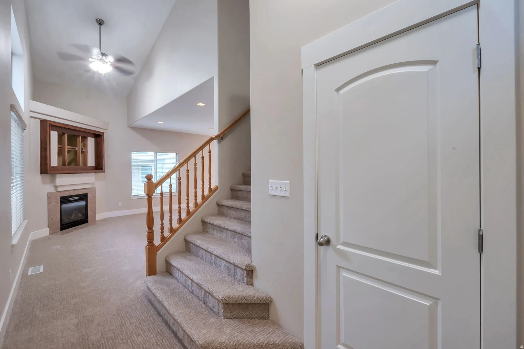 Vaulted ceiling with a ceiling fan, a fireplace with a wood mantel, carpeted flooring, and a wooden staircase