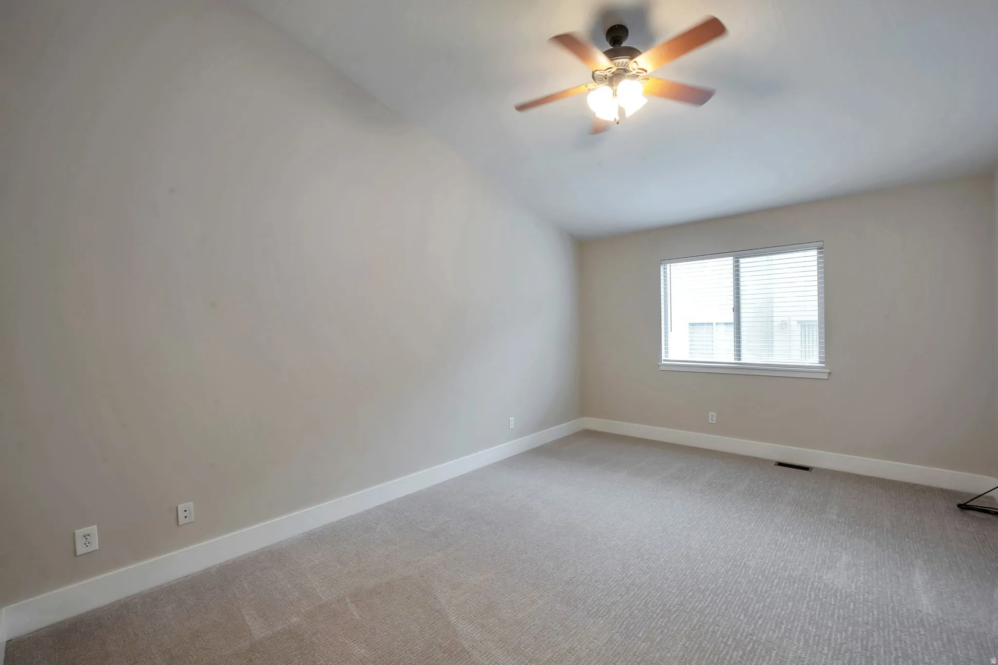 Primary bedroom with vaulted ceiling, ceiling fan with integrated lighting, neutral wall tones, window with horizontal blinds, carpeted flooring