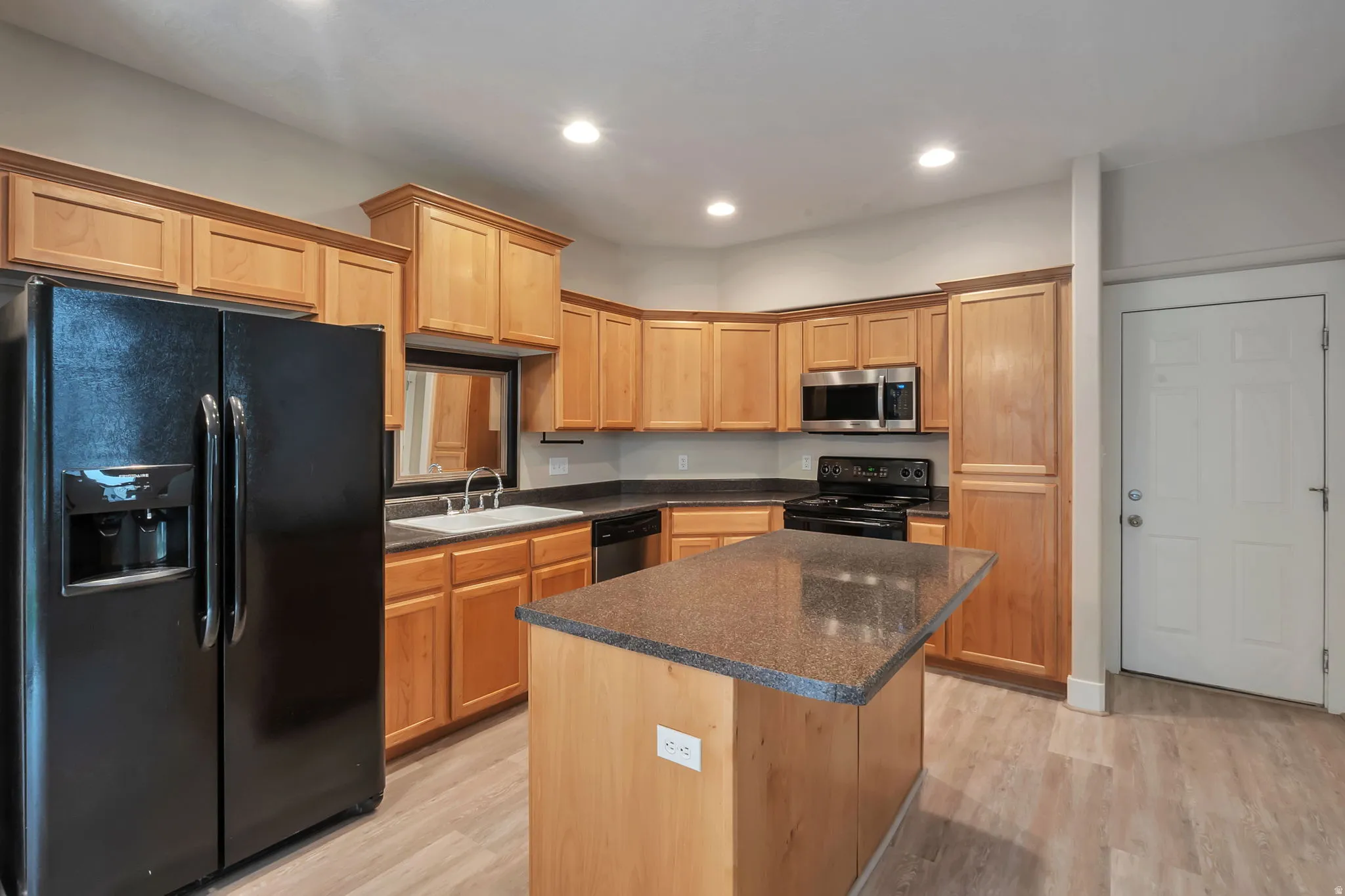 Kitchen featuring light wood cabinetry, dark countertops, a central island, recessed lighting, and LVP flooring