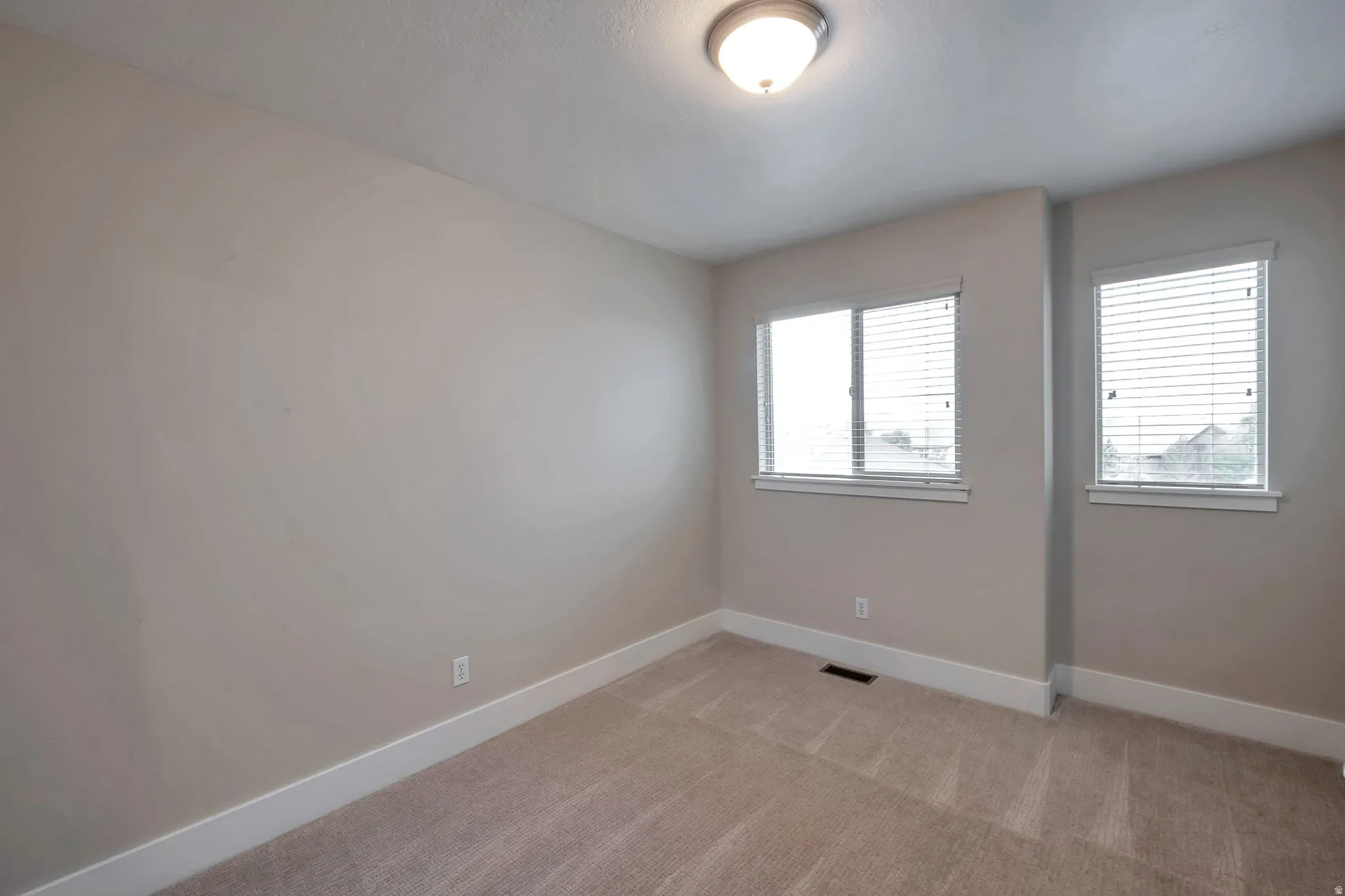 Wall-to-wall carpeting, two double-paned windows with blinds, flush mount ceiling light fixture, and neutral wall paint
