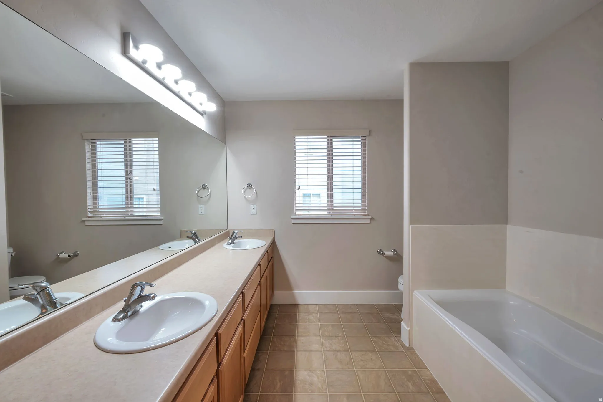 Primary bathroom with dual vanity with integrated sinks, expansive counter space, and light wood-finish cabinetry