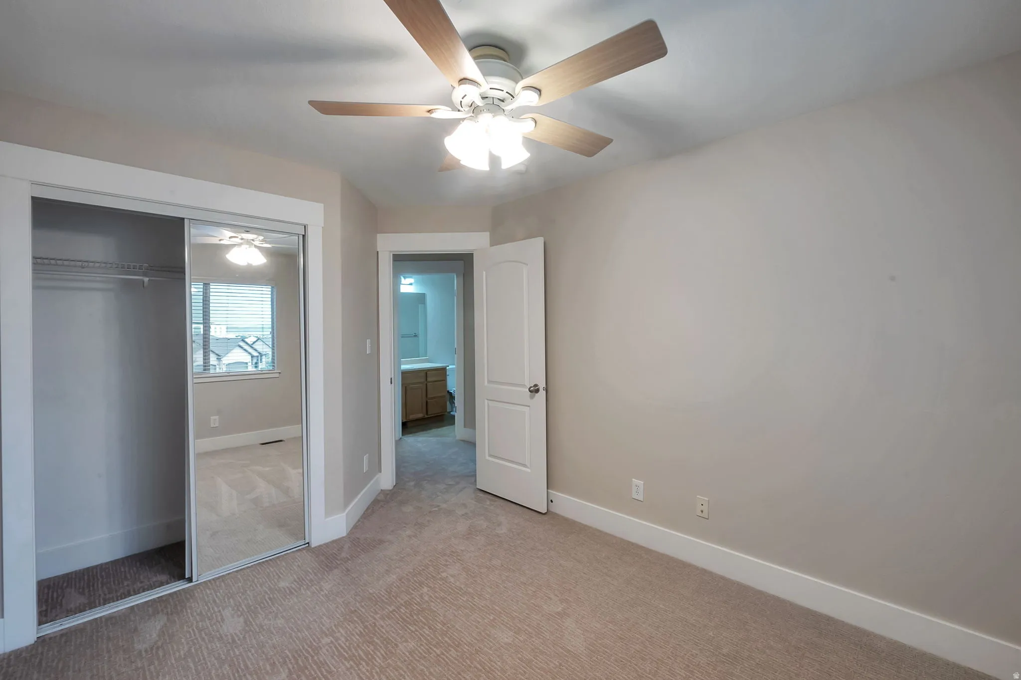Carpeted room featuring a ceiling fan with light fixture, mirrored sliding closet doors, and white trim