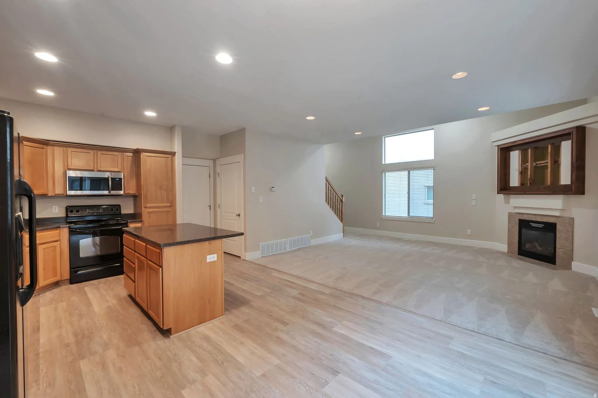 Open great room and kitchen with wood cabinetry, black appliances, and a central island