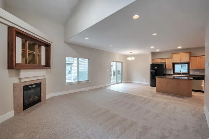 Great Room with vaulted ceiling, recessed lighting, fireplace with tile surround, wood-finish flooring, and sliding glass door