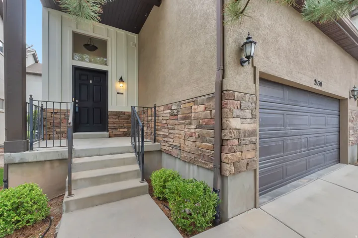 Stucco exterior with stone veneer accents, paneled garage door, and a covered entry with a black paneled door