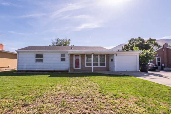 Exterior siding with brick accents, attached garage, front lawn, and mature trees