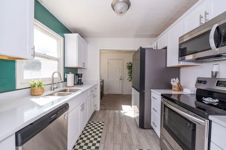 Contemporary kitchen featuring white cabinetry, light countertops, wood-finish flooring, a stainless steel dishwasher, and a stainless steel range with an overhead microwave