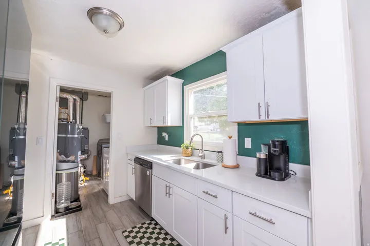 White cabinetry with brushed nickel hardware, stainless steel dishwasher, white countertops, single basin stainless steel sink with a gooseneck faucet, and wood-finish flooring