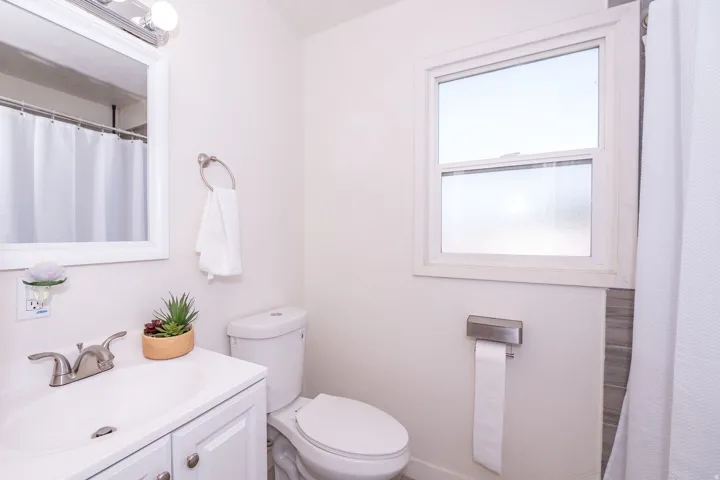 White vanity with a single basin, brushed nickel faucet, mirror with overhead lighting, and a window for natural illumination