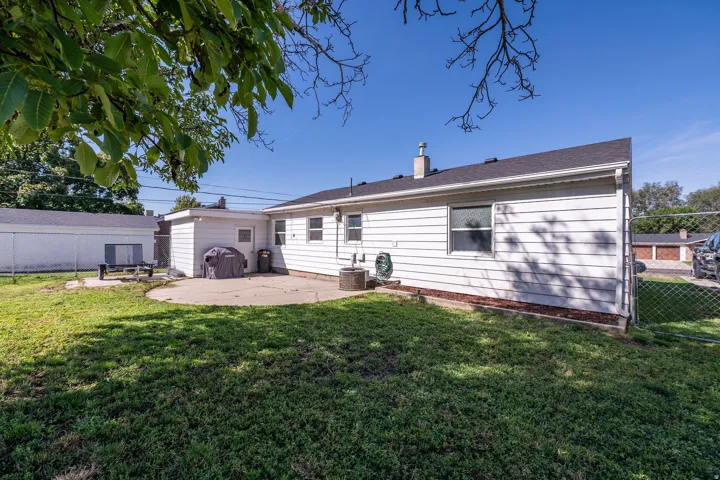Expansive backyard with a concrete patio, white horizontal siding, and a chain-link fence