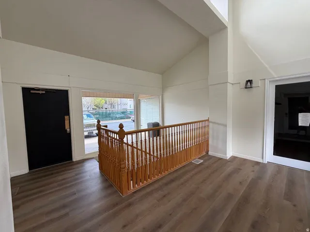 Wood-finish flooring, white walls, natural wood railing, large windows, and a vaulted ceiling